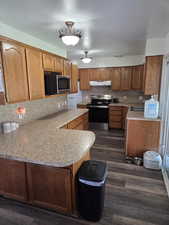 Kitchen with stainless steel appliances, under cabinet range hood, a peninsula, light countertops, and decorative backsplash