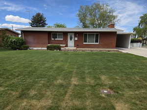 Single story home with a chimney, brick siding, a front yard, concrete driveway, and a carport