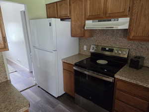 Kitchen with stainless steel range with electric cooktop, under cabinet range hood, freestanding refrigerator, backsplash, and dark wood-style flooring