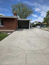 View of side of property with driveway, a chimney, an attached carport, brick siding, and fence