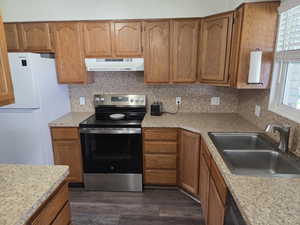 Kitchen featuring under cabinet range hood, stainless steel range with electric cooktop, freestanding refrigerator, a sink, and dark wood-type flooring