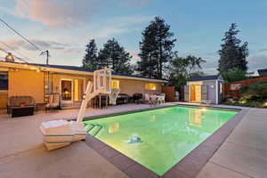 Pool at dusk featuring a patio area, a shed, fence, an outbuilding, and an outdoor hangout area