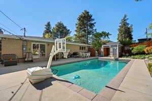View of swimming pool with a patio, a shed, fence, an outbuilding, and a diving board
