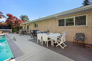 View of patio / terrace featuring outdoor dining area, a hot tub, a wooden deck, and an outdoor pool