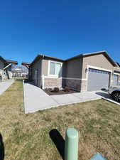View of front facade with an attached garage, stucco siding, a front lawn, and stone siding