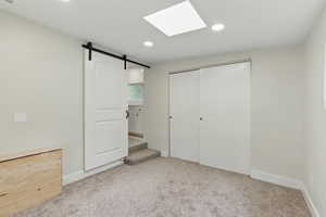 Unfurnished bedroom with carpet flooring, a closet, recessed lighting, a barn door, and baseboards