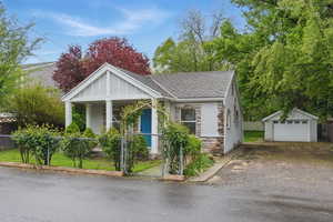 Bungalow with a fenced front yard, stone siding, an outdoor structure, and a garage
