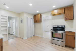 Kitchen featuring stainless steel range with electric cooktop, light wood finished floors, brown cabinetry, light countertops, and recessed lighting