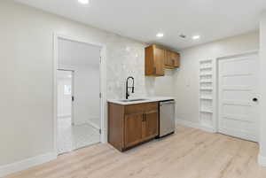 Kitchen with a sink, dishwasher, light countertops, light wood-style flooring, and recessed lighting