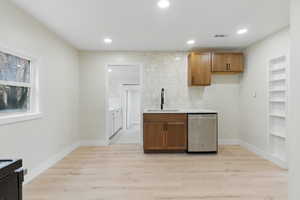 Kitchen featuring a sink, stainless steel dishwasher, light wood-type flooring, brown cabinets, and recessed lighting