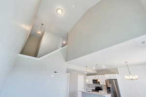Detailed view of stainless steel appliances, light countertops, white cabinets, a center island with sink, and pendant lighting