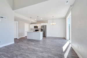 Unfurnished living room with a chandelier, baseboards, wood finished floors, and recessed lighting