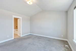 Unfurnished bedroom with light carpet, vaulted ceiling, baseboards, and ensuite bathroom