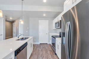 Kitchen featuring stainless steel appliances, a sink, light countertops, white cabinets, and pendant lighting