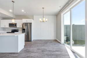 Kitchen with appliances with stainless steel finishes, a chandelier, light wood-type flooring, white cabinets, and light countertops