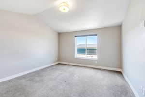 Carpeted spare room with vaulted ceiling and baseboards