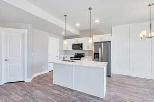 Kitchen with stainless steel appliances, white cabinets, light countertops, a kitchen island with sink, and a chandelier