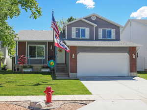 View of front of property with an attached garage, a front yard, concrete driveway, brick siding, and roof with shingles