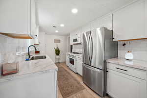 Kitchen featuring white appliances, a sink, backsplash, light wood-style flooring, and recessed lighting