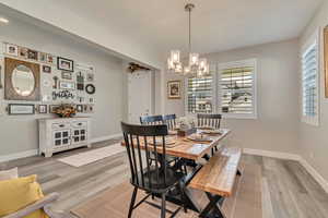 Dining space with a chandelier, wood-like laminate floors, and baseboards