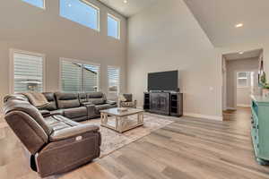 Living area featuring baseboards, light wood-like laminate flooring, a towering ceiling, and recessed lighting