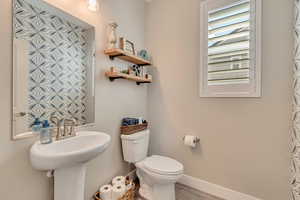 Bathroom with toilet, baseboards, wood-like laminate floors, and a sink