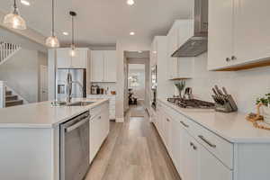 Kitchen with wall chimney range hood, appliances with stainless steel finishes, a sink, recessed lighting, and light wood-like laminate flooring