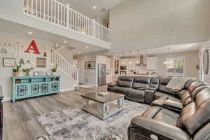 Living room featuring light wood-like laminate flooring, stairway, a high ceiling, baseboards, and a chandelier
