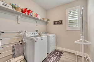 Clothes washing area with washing machine and clothes dryer, light wood-like laminate floors, and baseboards
