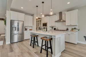 Kitchen featuring stainless steel refrigerator with ice dispenser, wall chimney exhaust hood, built in microwave, a sink, and recessed lighting