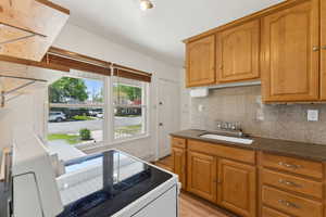 Kitchen featuring a sink, light wood-style floors, tasteful backsplash, dark stone counters, and brown cabinets