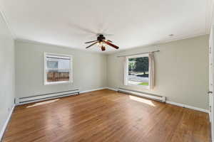 Living room with baseboard heating, a ceiling fan, ornamental molding, hardwood / wood-style flooring, and baseboards