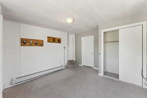 Unfurnished bedroom with baseboard heating, carpet flooring, a closet, and baseboards