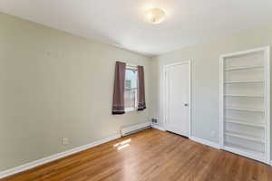 Unfurnished bedroom with a baseboard radiator, wood finished floors, and baseboards