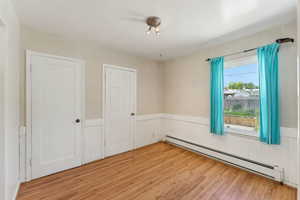 Spare room with a baseboard heating unit, light wood-style floors, and a wainscoted wall