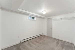 Basement featuring a baseboard heating unit and light carpet