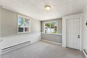 Spare room with a baseboard heating unit, a baseboard radiator, carpet, plenty of natural light, and a textured ceiling
