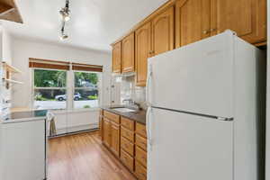 Kitchen featuring freestanding refrigerator, a baseboard heating unit, a sink, light wood-style floors, and brown cabinetry