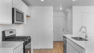 Kitchen featuring appliances with stainless steel finishes, a sink, light countertops, light wood-style flooring, and white cabinetry