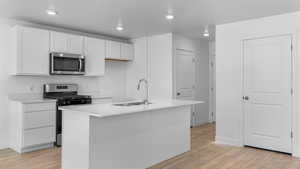 Kitchen featuring stainless steel appliances, a sink, light wood finished floors, white cabinetry, and light countertops