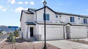 Townhome / multi-family property featuring a garage, driveway, a shingled roof, and stone siding