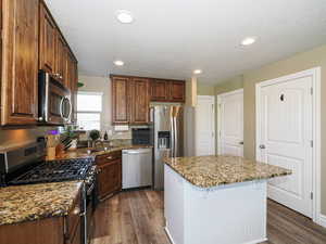 Kitchen featuring appliances with stainless steel finishes, dark wood-style flooring, a kitchen breakfast bar, a sink, and stone counters