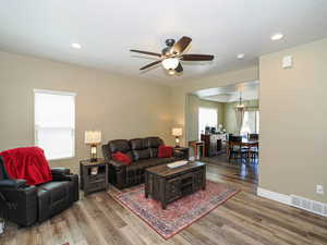 Living area featuring wood finished floors, a ceiling fan, a chandelier, baseboards, and recessed lighting