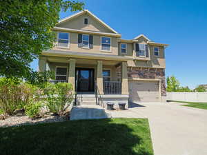 View of front facade with a porch, stucco siding, driveway, stone siding, and an attached garage