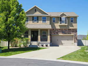 View of front of home with stucco siding, stone siding, a garage, concrete driveway, and a porch