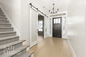 Entryway with a barn door, stairs, light wood-style floors, a chandelier, and baseboards