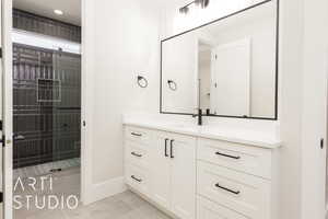 Bathroom with vanity, baseboards, tile patterned floors, and a tile shower