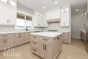Kitchen with light countertops, light wood finished floors, backsplash, glass insert cabinets, and recessed lighting