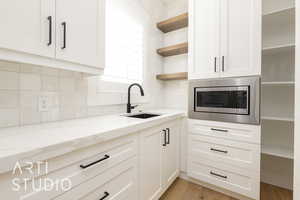 Kitchen with open shelves, stainless steel microwave, a sink, tasteful backsplash, and light stone counters