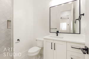 Bathroom with toilet, vanity, a tile shower, and baseboards